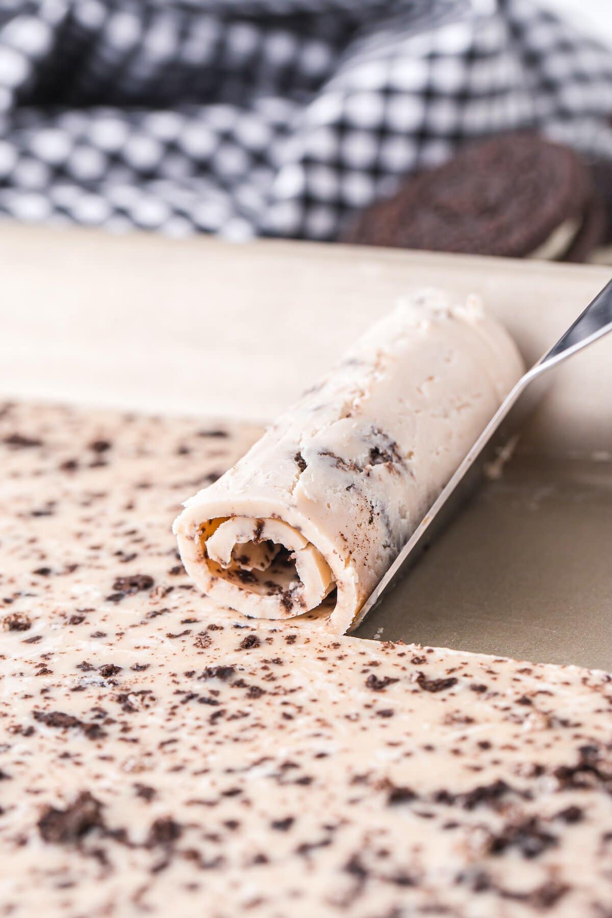 Freshly rolled Oreo ice cream being lifted from the frozen pan with a spatula.
