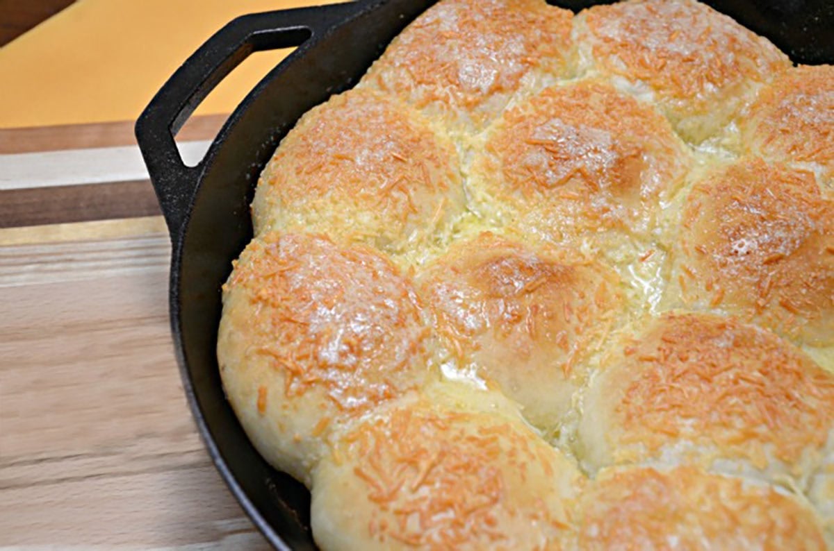 Cast iron skillet filled with golden stuffed parmesan rolls baked together, topped with melted parmesan cheese on a wooden cutting board.