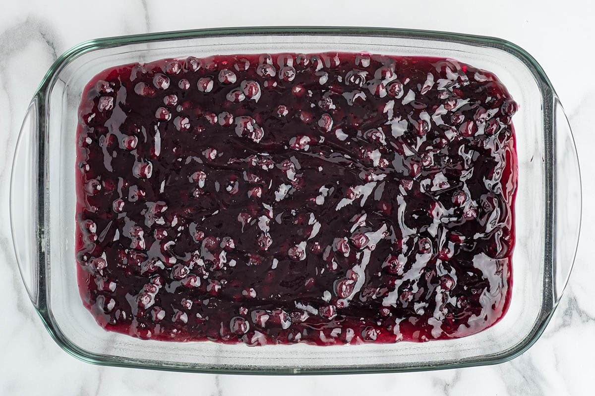 Blueberry pie filling spread in a glass baking dish as the first layer of dump cake.
