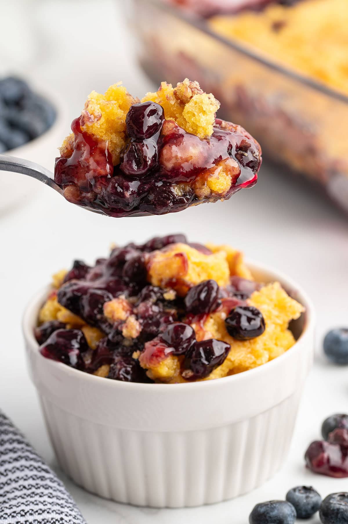Spoonful of blueberry dump cake held over a white ramekin filled with cake and blueberry filling.