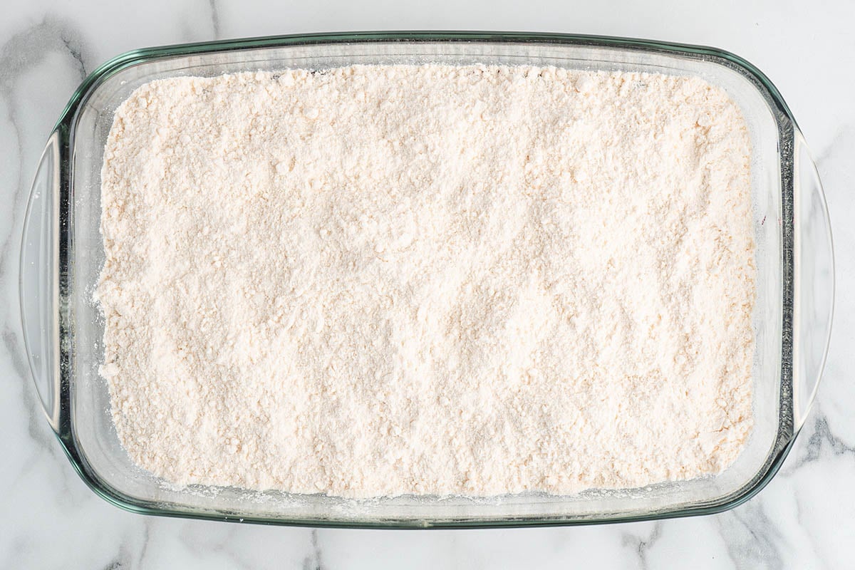 Dry yellow cake mix spread evenly over blueberry filling in a glass baking dish.