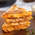 Stack of buffalo chicken quesadillas with melted cheese and shredded buffalo chicken in crispy toasted tortillas on a wooden board.