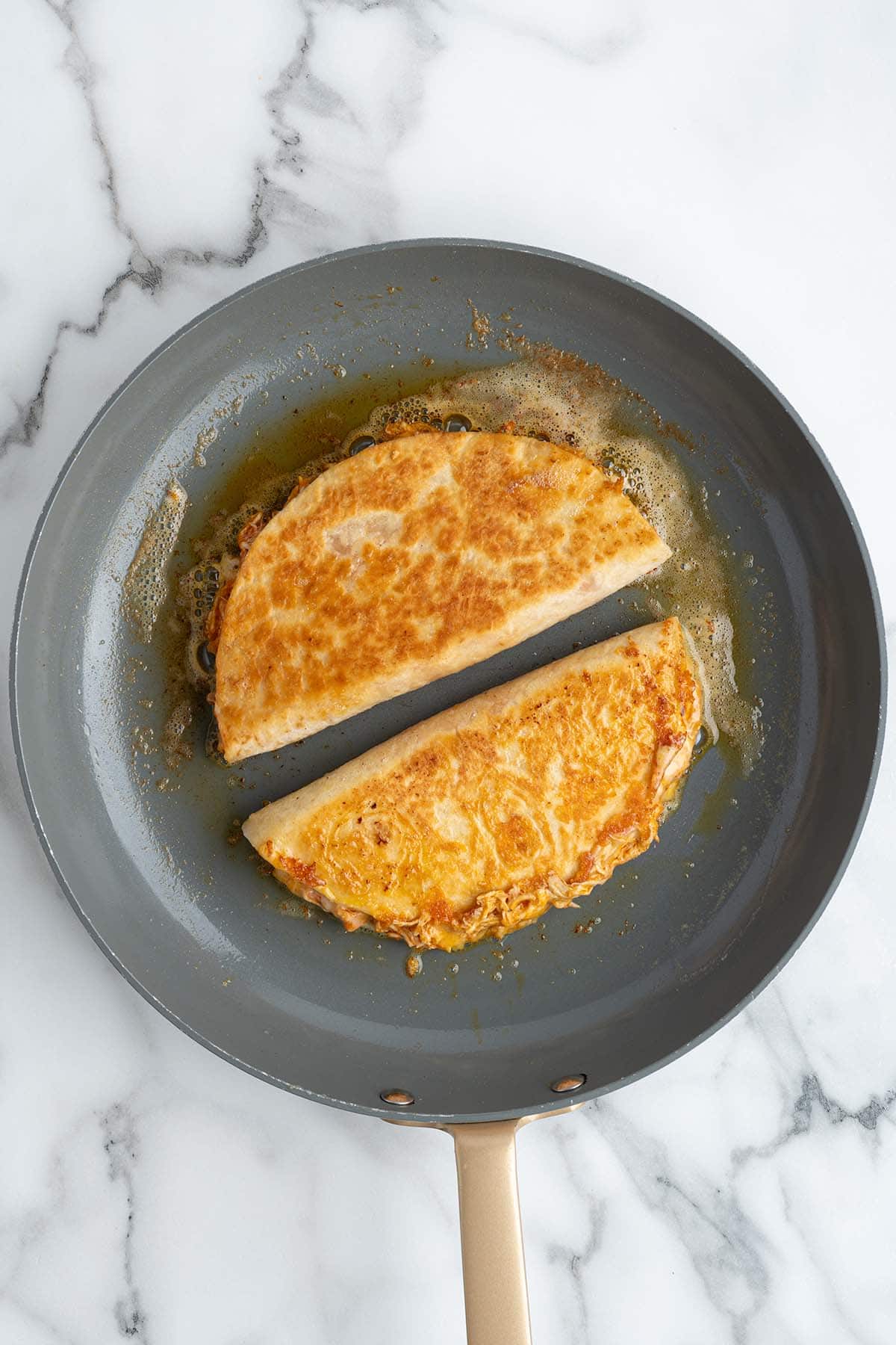 Overhead view of crispy buffalo chicken quesadillas cooking in a skillet with golden toasted tortillas and melted cheese inside.