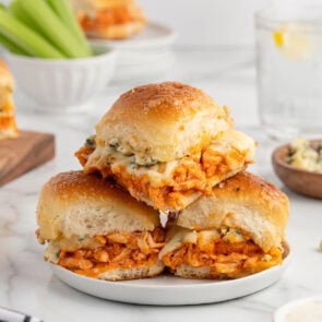Plate of buffalo chicken sliders made with shredded buffalo chicken, melted cheese, and soft toasted buns, stacked and ready to serve.