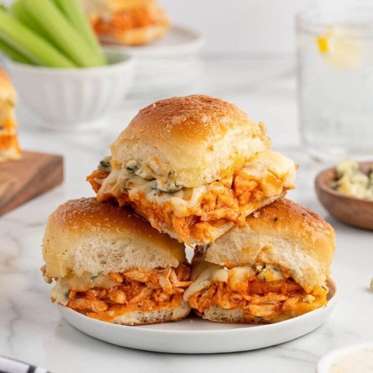 Plate of buffalo chicken sliders made with shredded buffalo chicken, melted cheese, and soft toasted buns, stacked and ready to serve.
