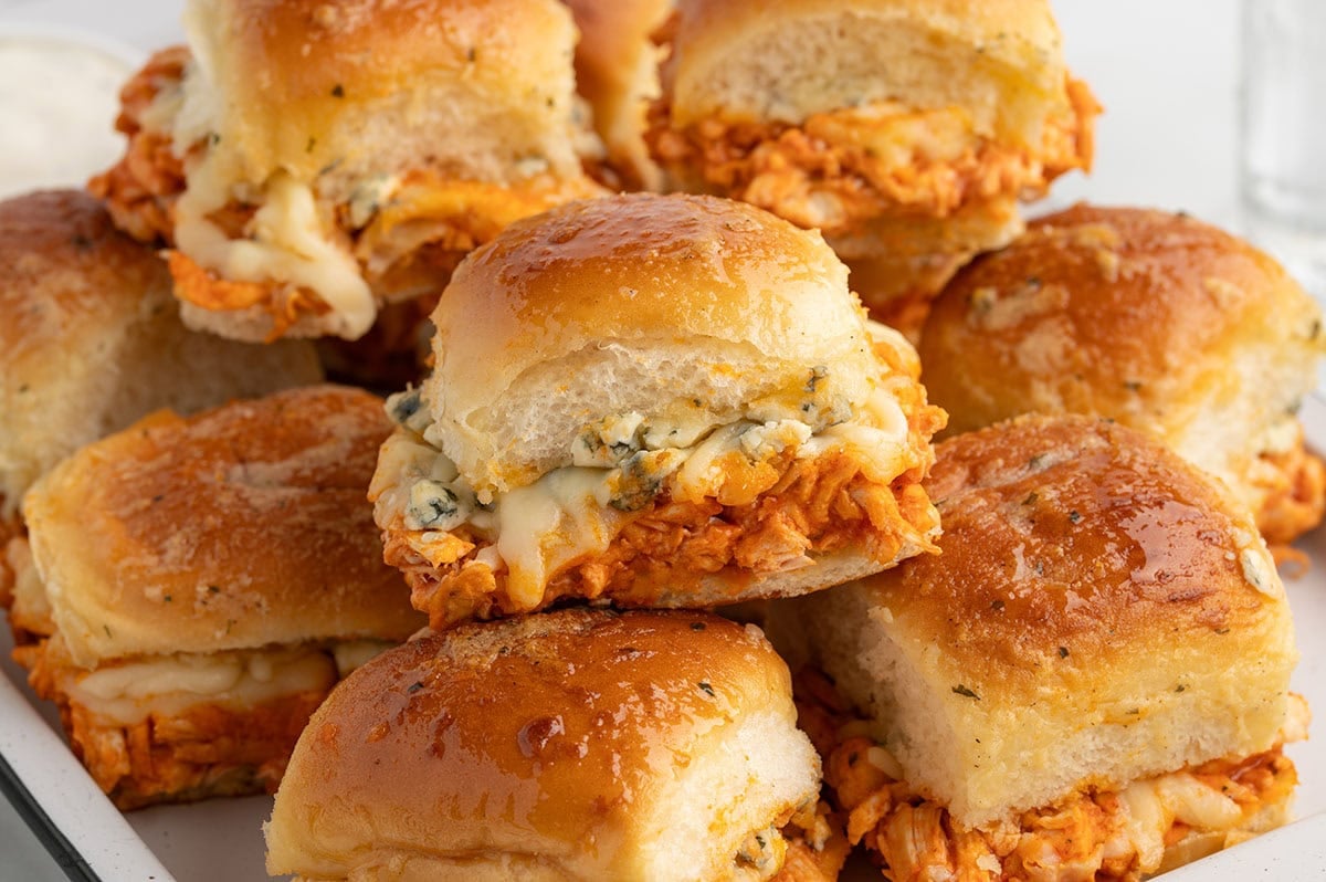 Close-up of baked buffalo chicken sliders topped with melted cheese and buffalo chicken on soft golden slider buns in a baking dish.