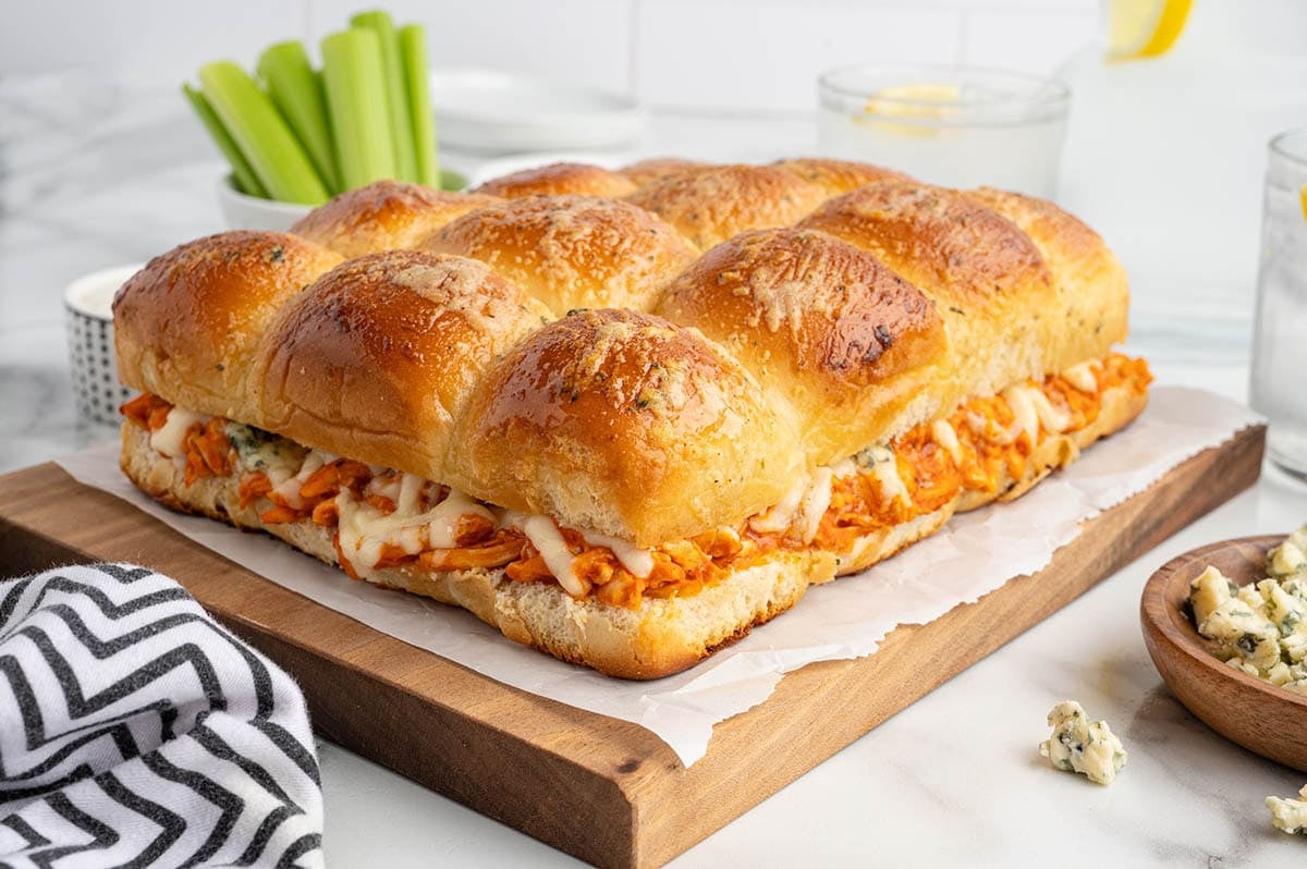 Tray of baked buffalo chicken sliders on soft golden buns filled with shredded buffalo chicken and melted cheese, served on a wooden board.