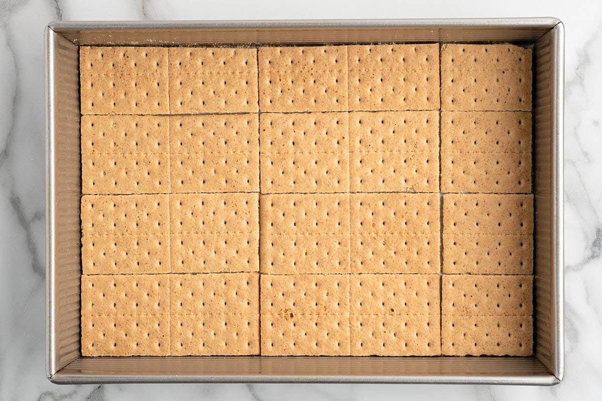 Top-down shot of graham crackers arranged in a baking dish to form the base layer for caramel apple eclair cake.