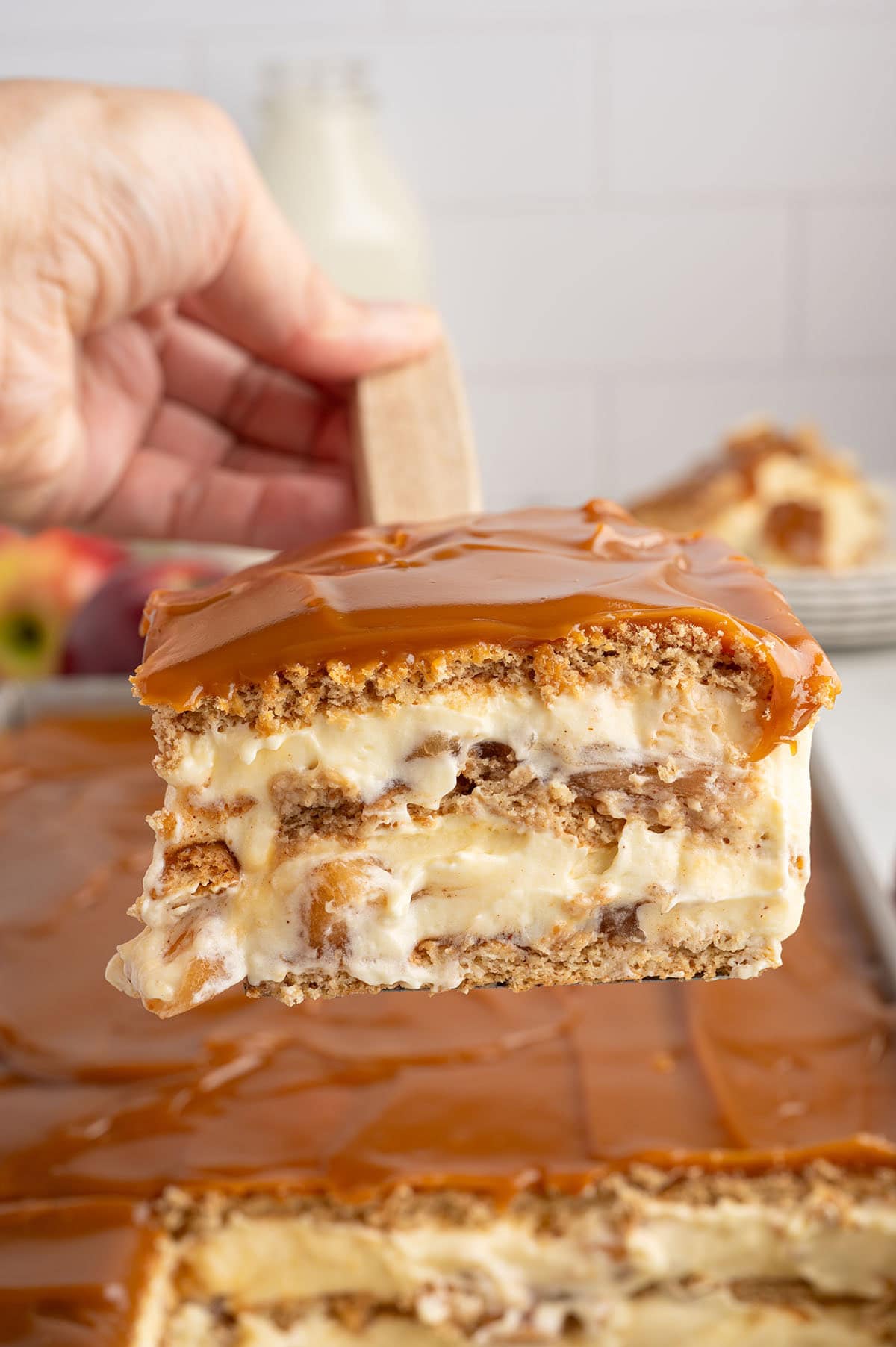 Close-up of a slice of caramel apple eclair cake with creamy layers, apples, graham crackers, and a thick caramel topping.