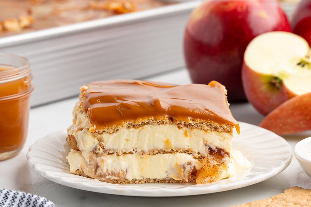 Slice of caramel apple eclair cake layered with creamy filling, apples, graham crackers, and a smooth caramel topping.