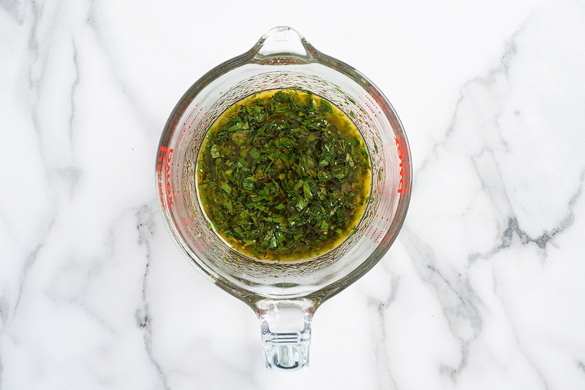Herb vinaigrette dressing with fresh chopped herbs in a glass measuring cup.