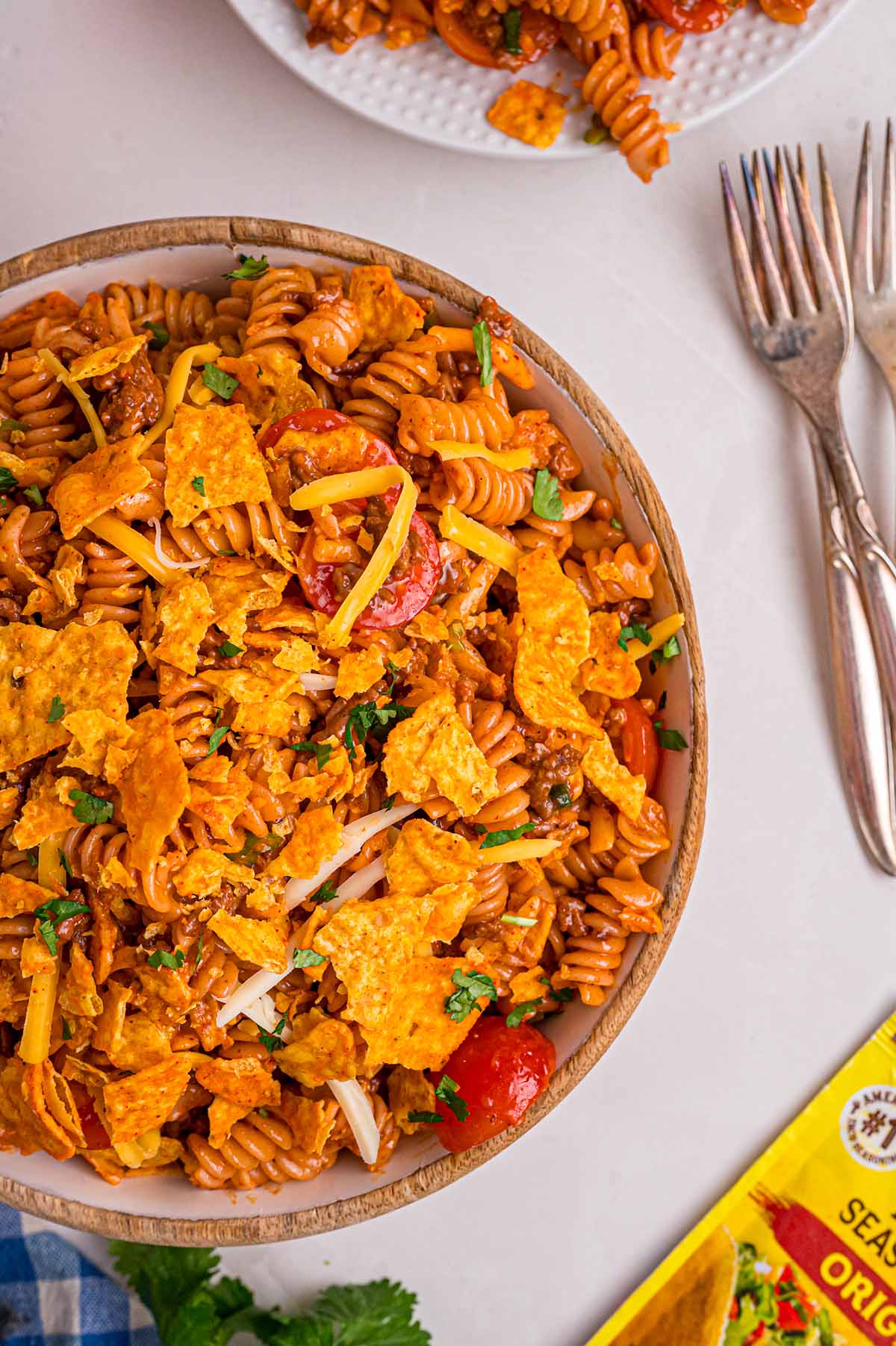 Overhead close-up of Doritos pasta salad with rotini, crushed Doritos, cherry tomatoes, and shredded cheese in a wooden bowl.