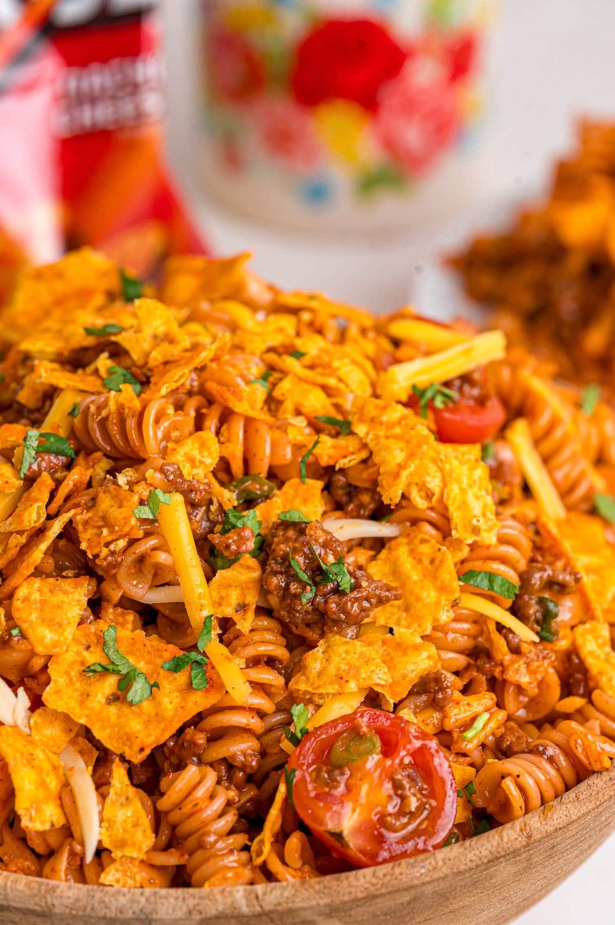 Close-up of Doritos pasta salad with rotini, ground beef, cherry tomatoes, shredded cheese, and Dorito chips garnished with cilantro.