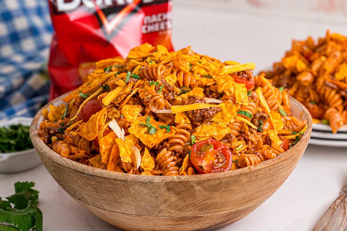 Doritos pasta salad with rotini, ground beef, cherry tomatoes, cheddar, and crushed nacho cheese Doritos in a wooden bowl.