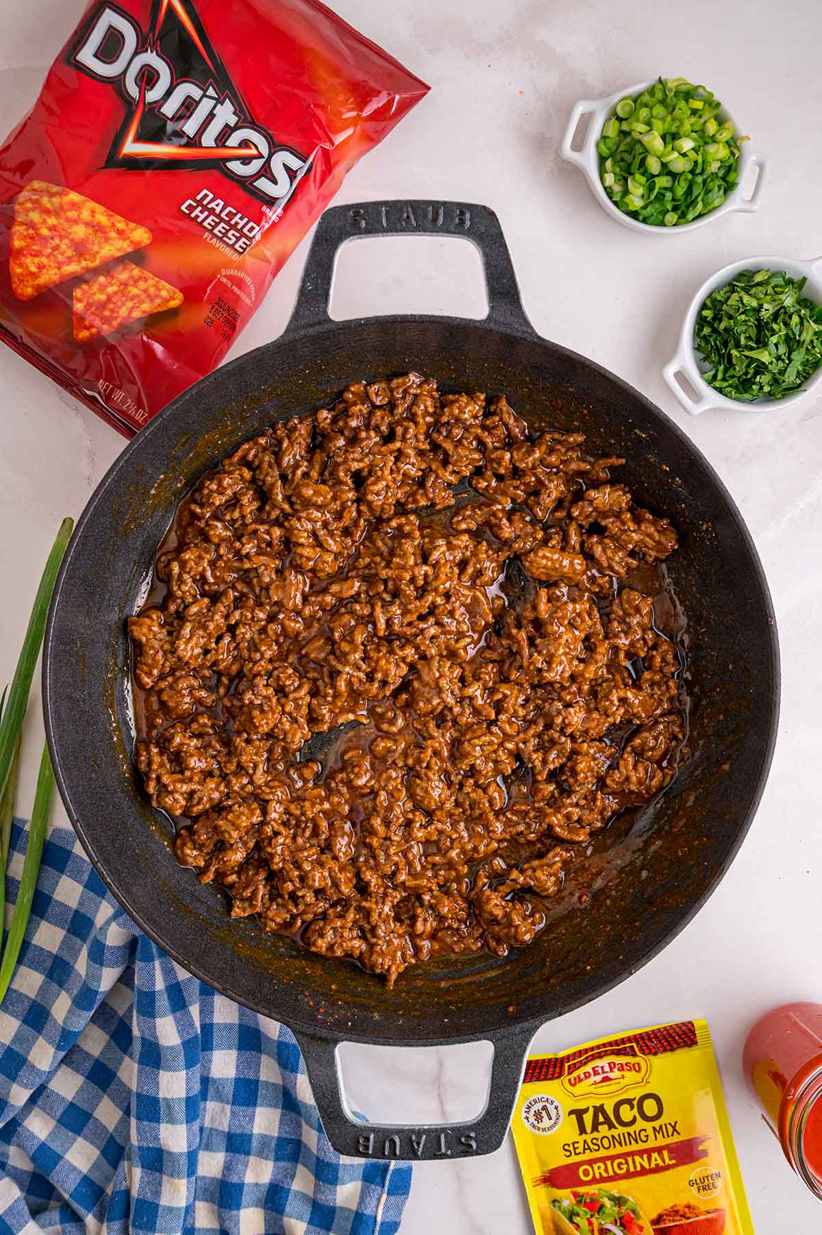 Taco-seasoned ground beef cooking in a cast iron skillet with a bag of Doritos and taco seasoning packet nearby.