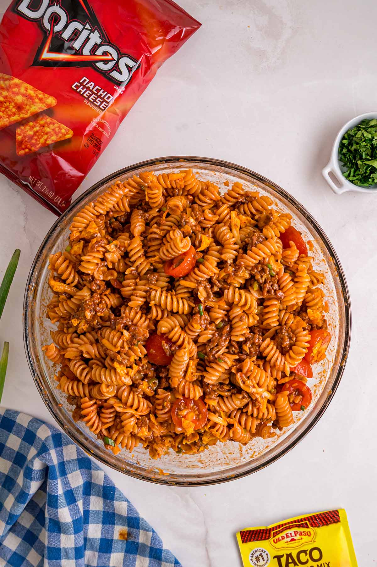 Overhead view of fully mixed Doritos pasta salad with rotini, ground beef, and cherry tomatoes in a glass bowl.