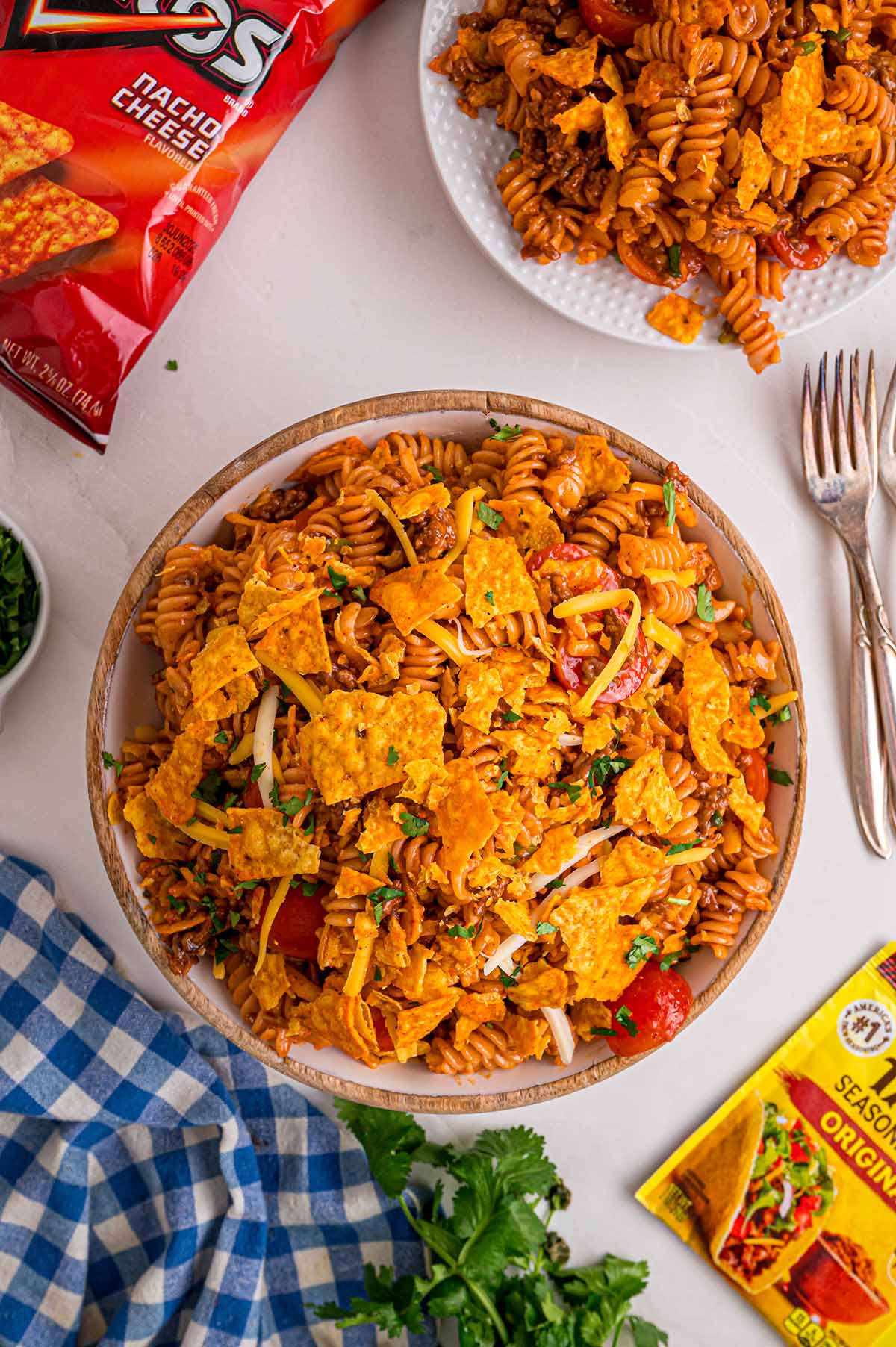 Overhead view of Doritos pasta salad topped with whole Dorito chips, shredded cheese, and cilantro in a wooden bowl.