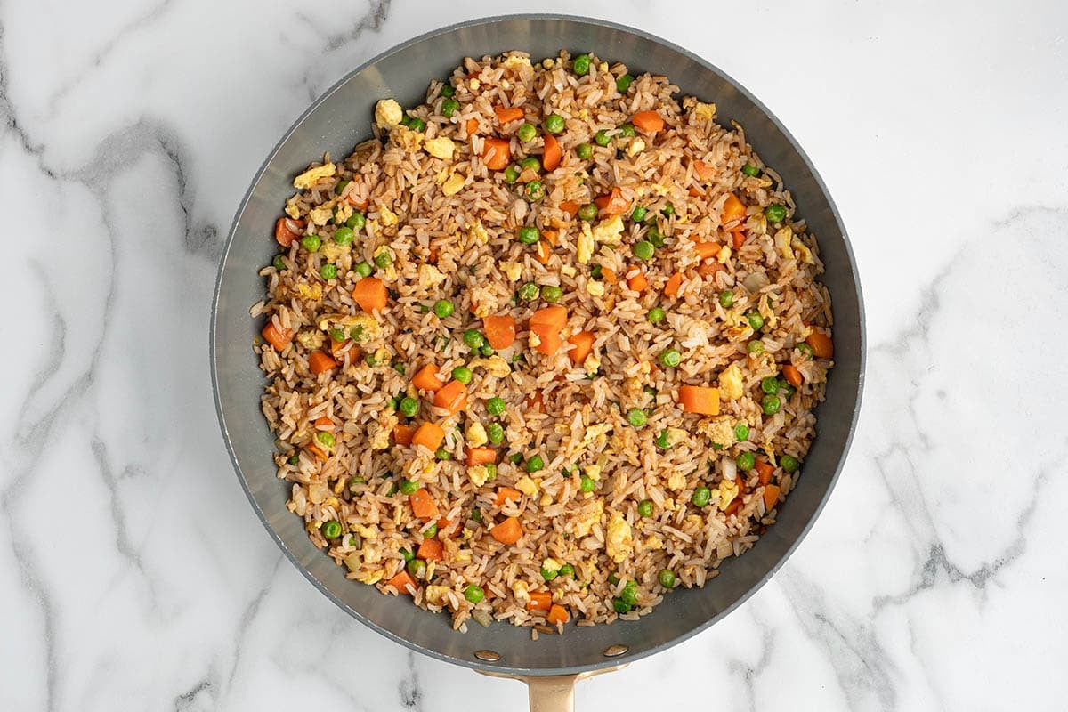 Overhead view of finished homemade fried rice with carrots, peas, scrambled eggs, and onions cooked in a skillet with soy sauce seasoning.