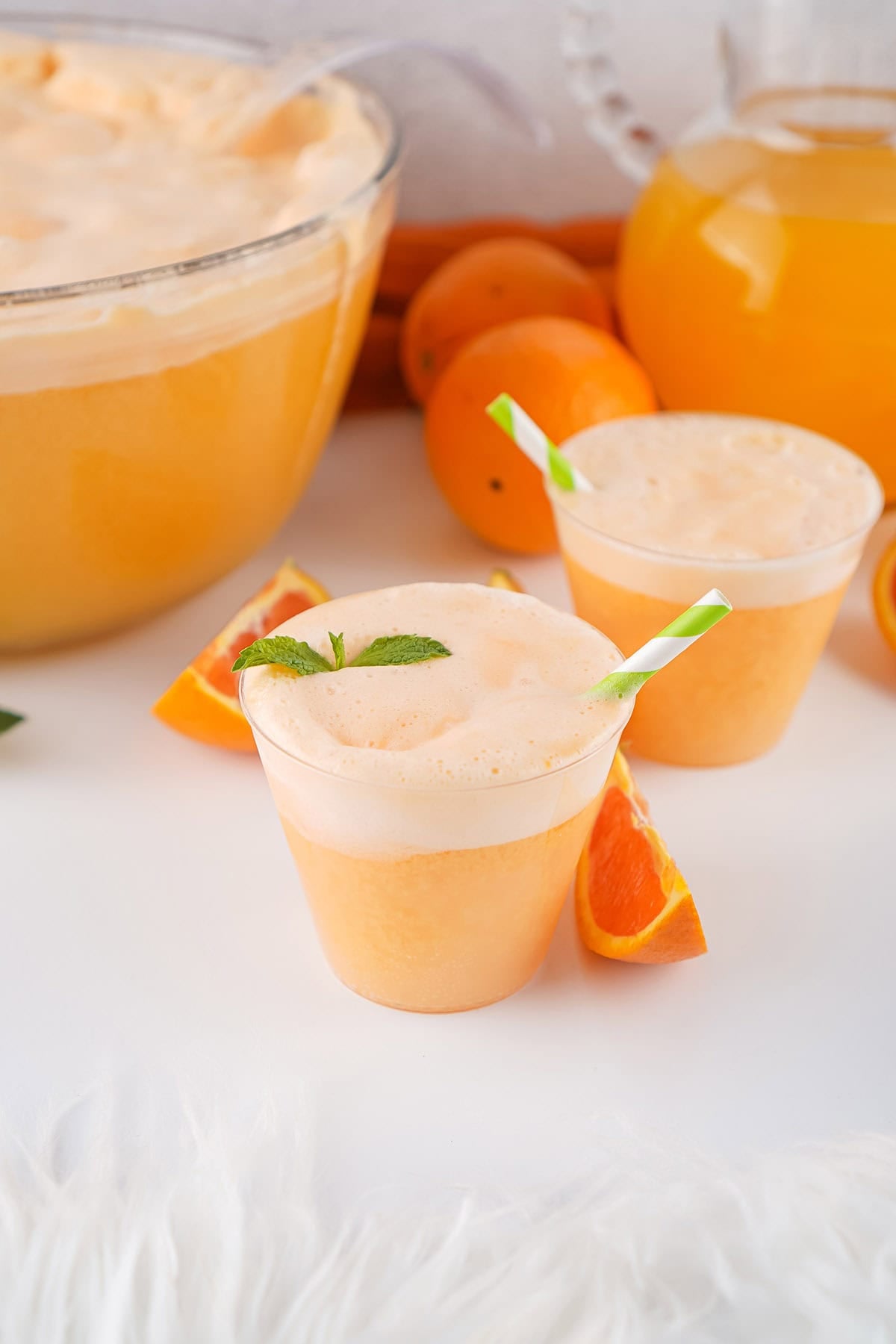 Glasses of creamy orange punch with frothy topping, orange slices, and mint garnish.