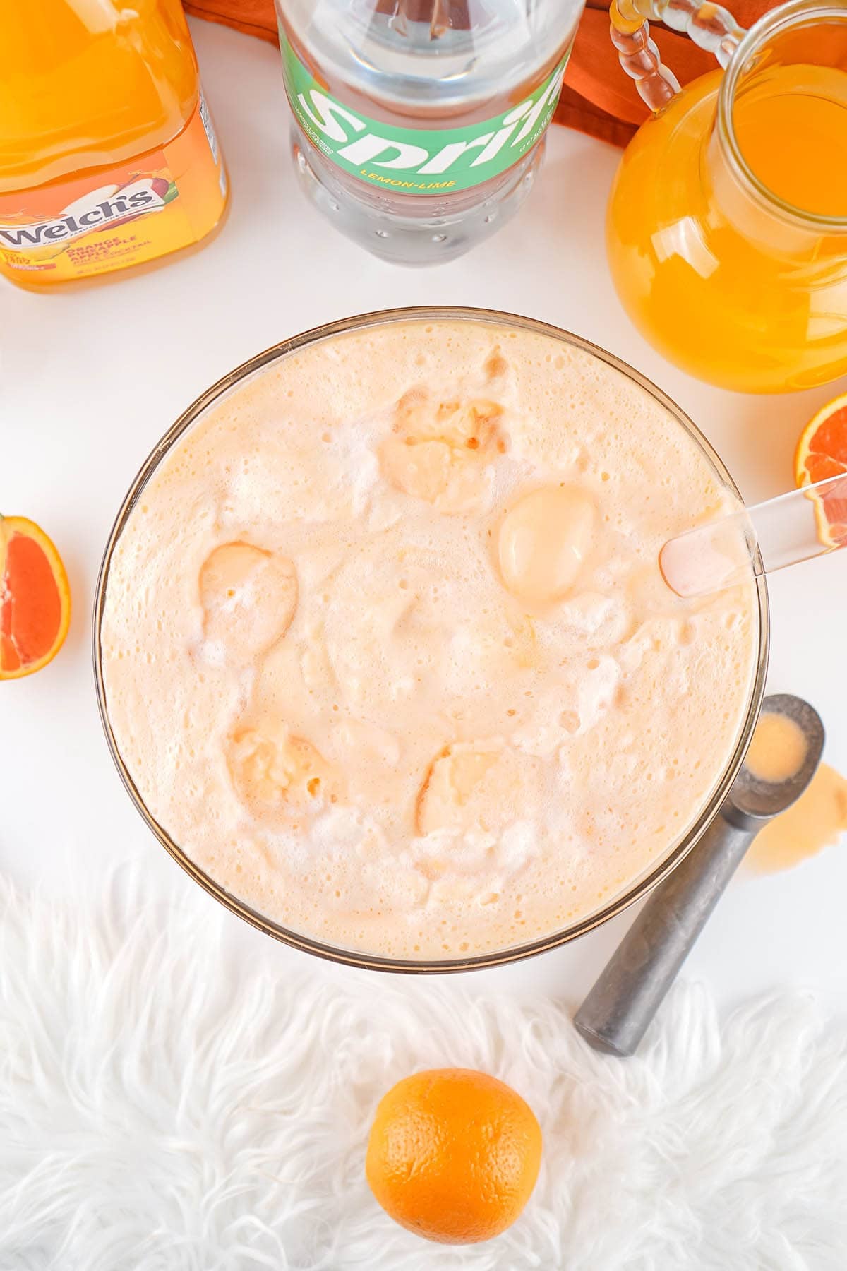 Top view of creamy orange punch in a glass bowl with orange slices and citrus drinks nearby.