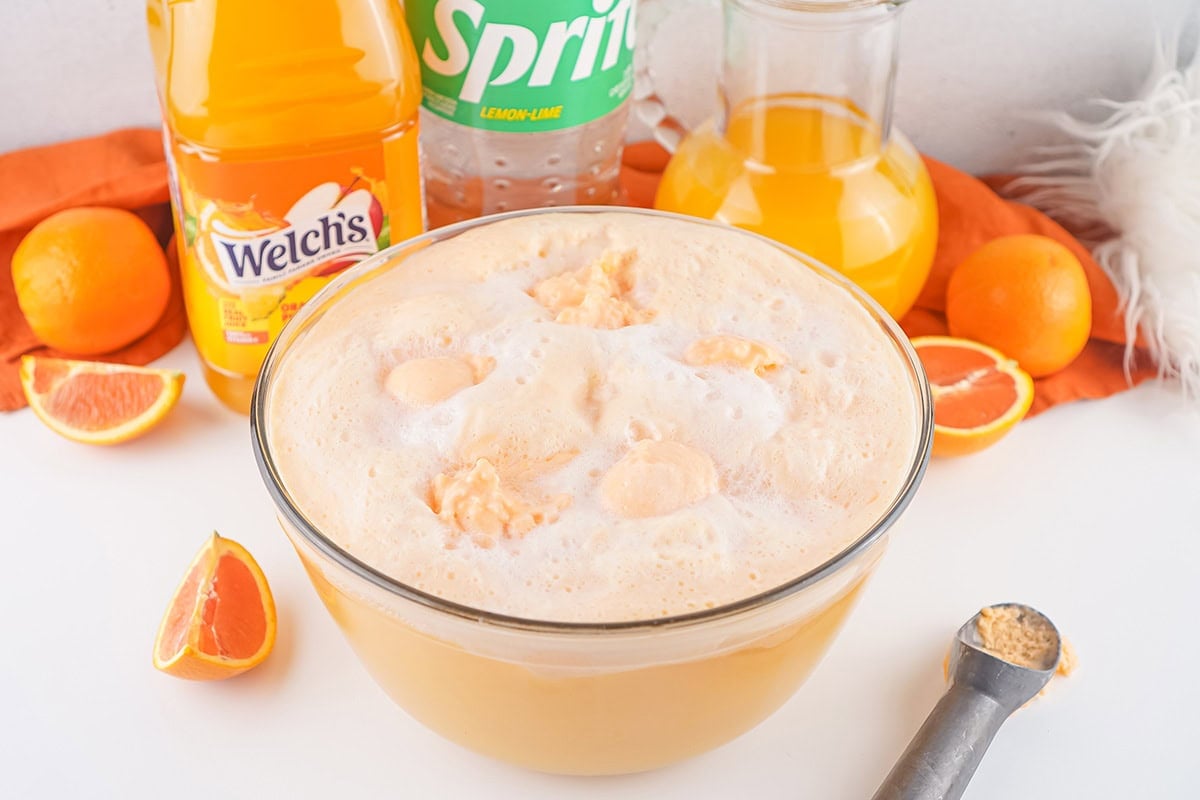 Creamy orange punch in a glass bowl with sliced oranges and citrus drinks in the background.