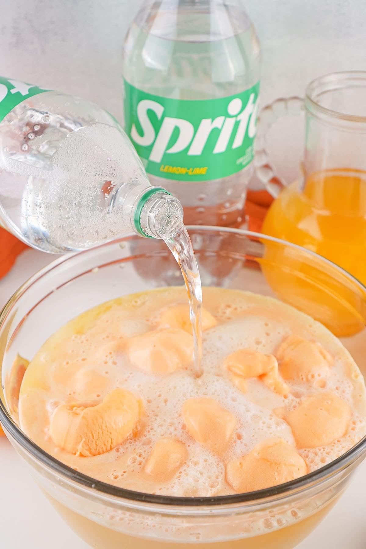 Pouring Sprite into creamy orange sherbet punch in a glass bowl.