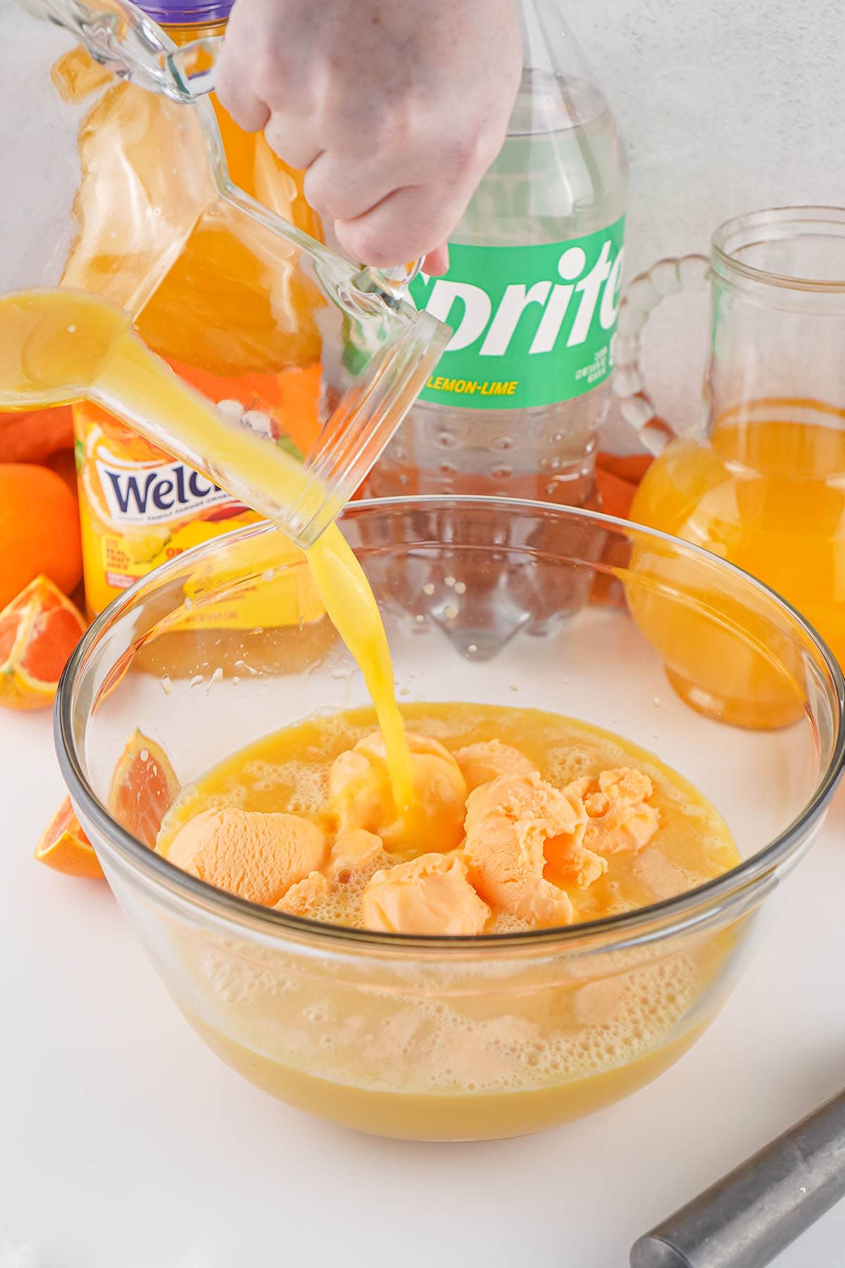 Orange punch being pour over scoops of orange sherbet in glass bowl.