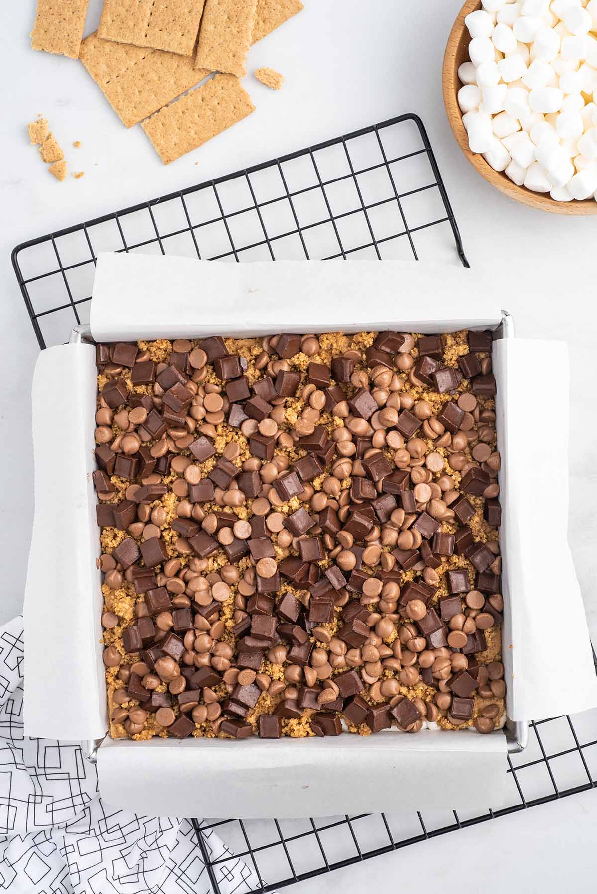 Top-down shot of oven-baked s’mores bars layered with chocolate chunks and chips over graham crackers.