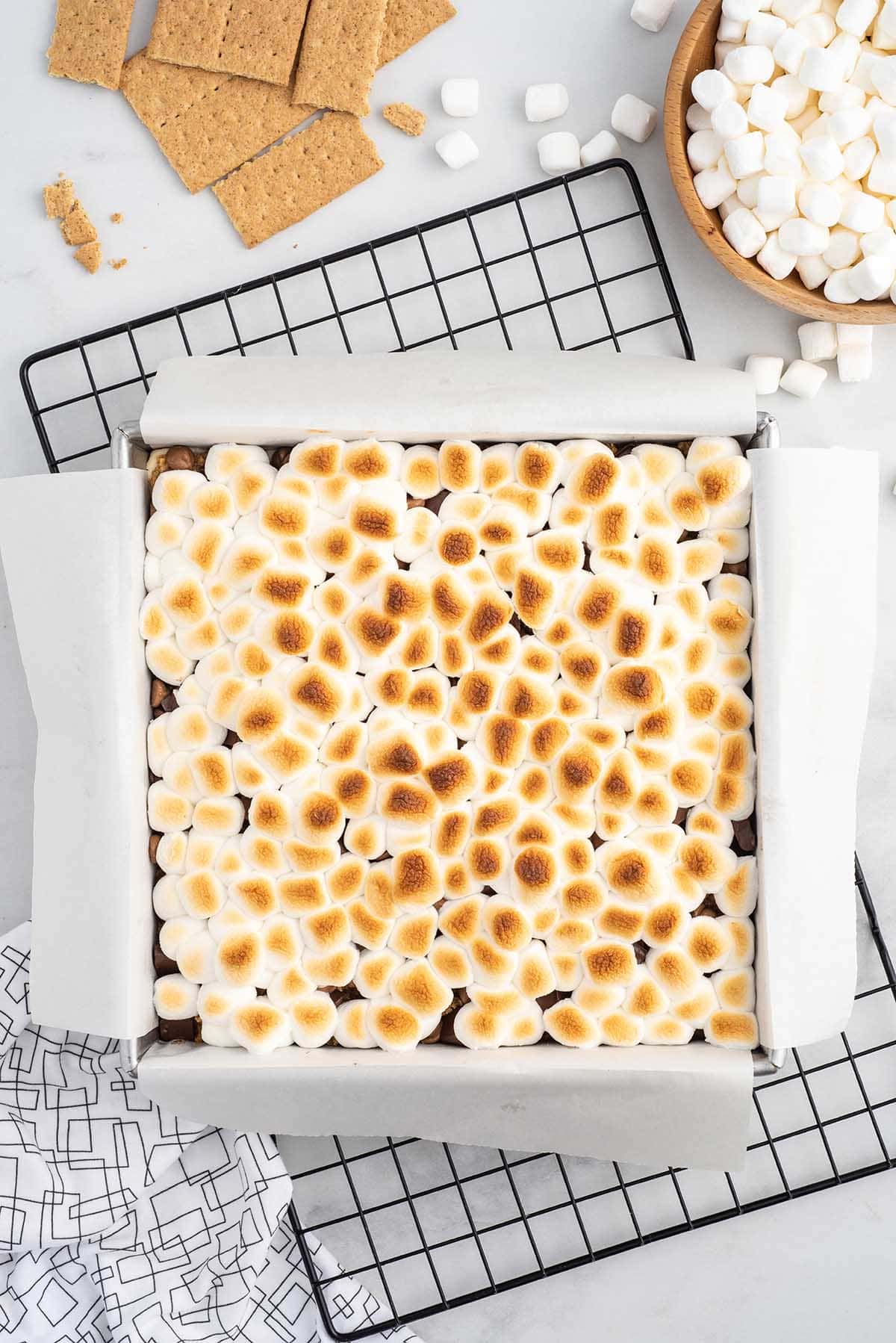 Top-down shot of toasted marshmallows baked over layers of chocolate for oven-baked s’mores bars.