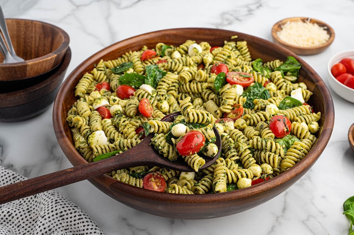 Pesto pasta salad tossed with mozzarella, spinach, and juicy cherry tomatoes in a large serving bowl.