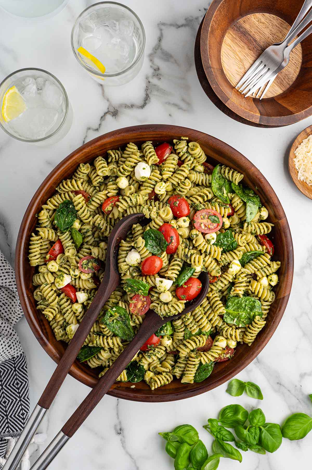 Overhead view of fresh pesto pasta salad with rotini, mozzarella pearls, spinach, and cherry tomatoes.