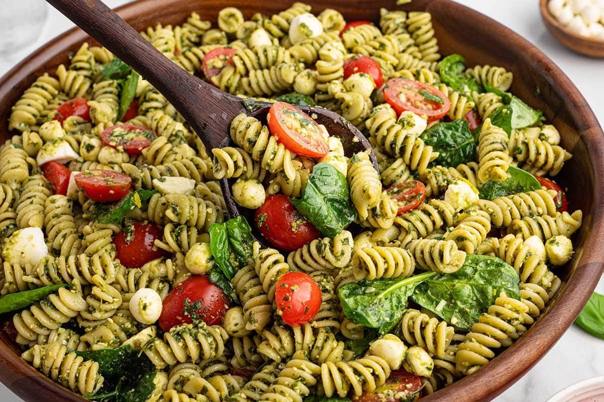Colorful pesto pasta salad tossed with rotini, spinach, mozzarella pearls, and juicy cherry tomatoes.