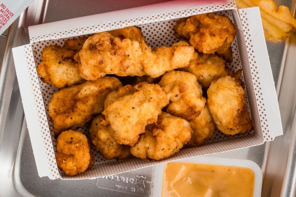 Copycat Chick-fil-A chicken nuggets in a paper tray with a side of dipping sauce on a metal tray.