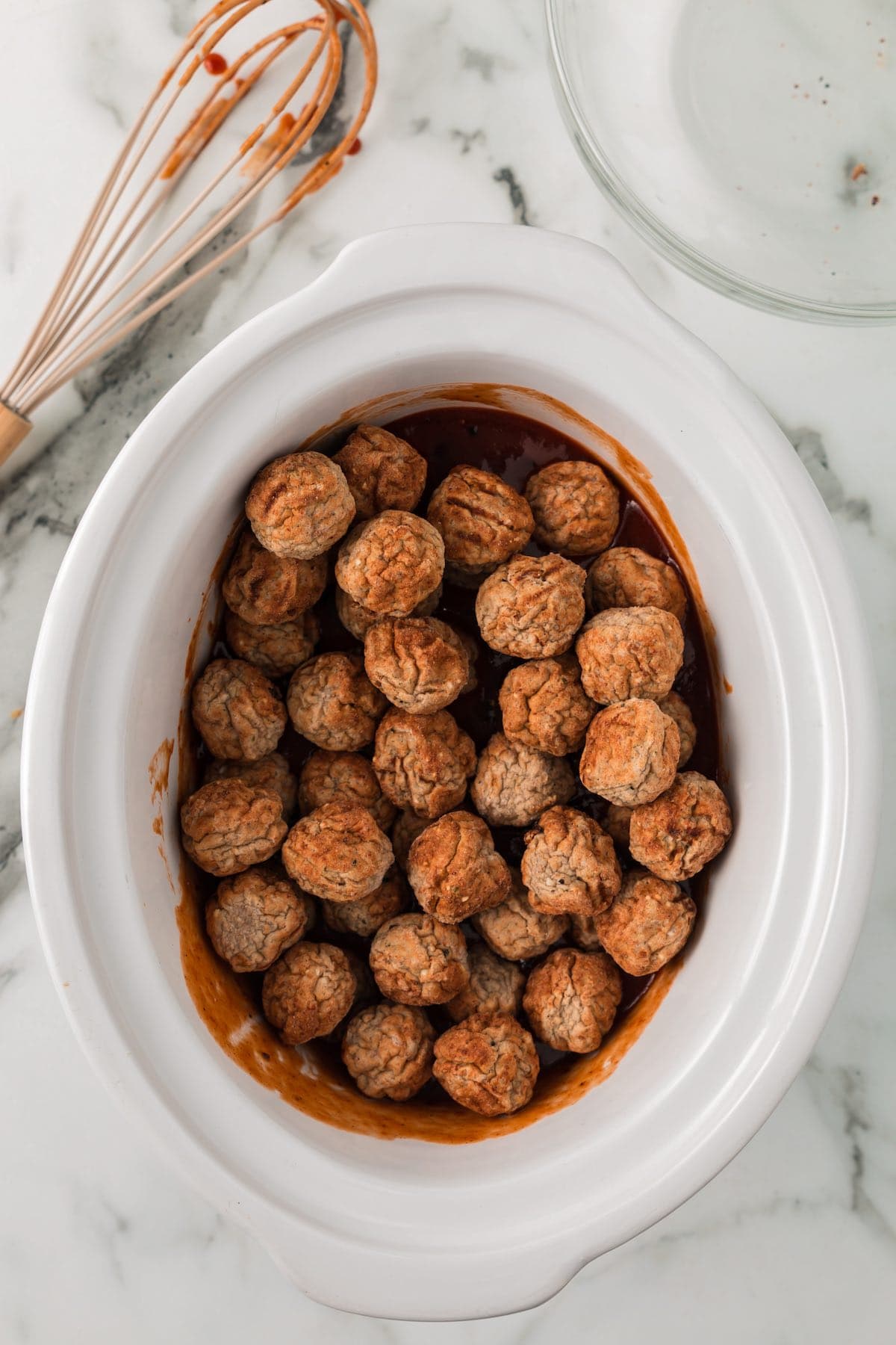 Frozen meatballs added to a slow cooker with grape jelly barbecue sauce before cooking.