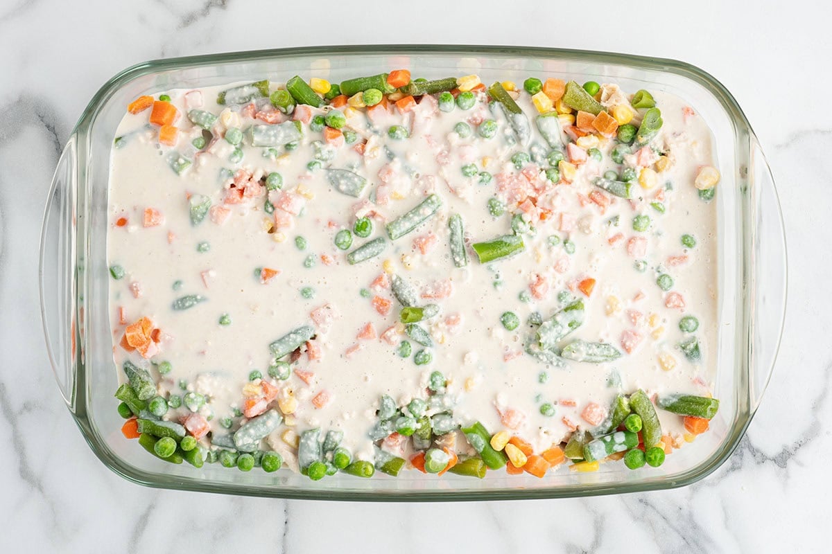 Cream sauce poured over vegetables and chicken in a baking dish.