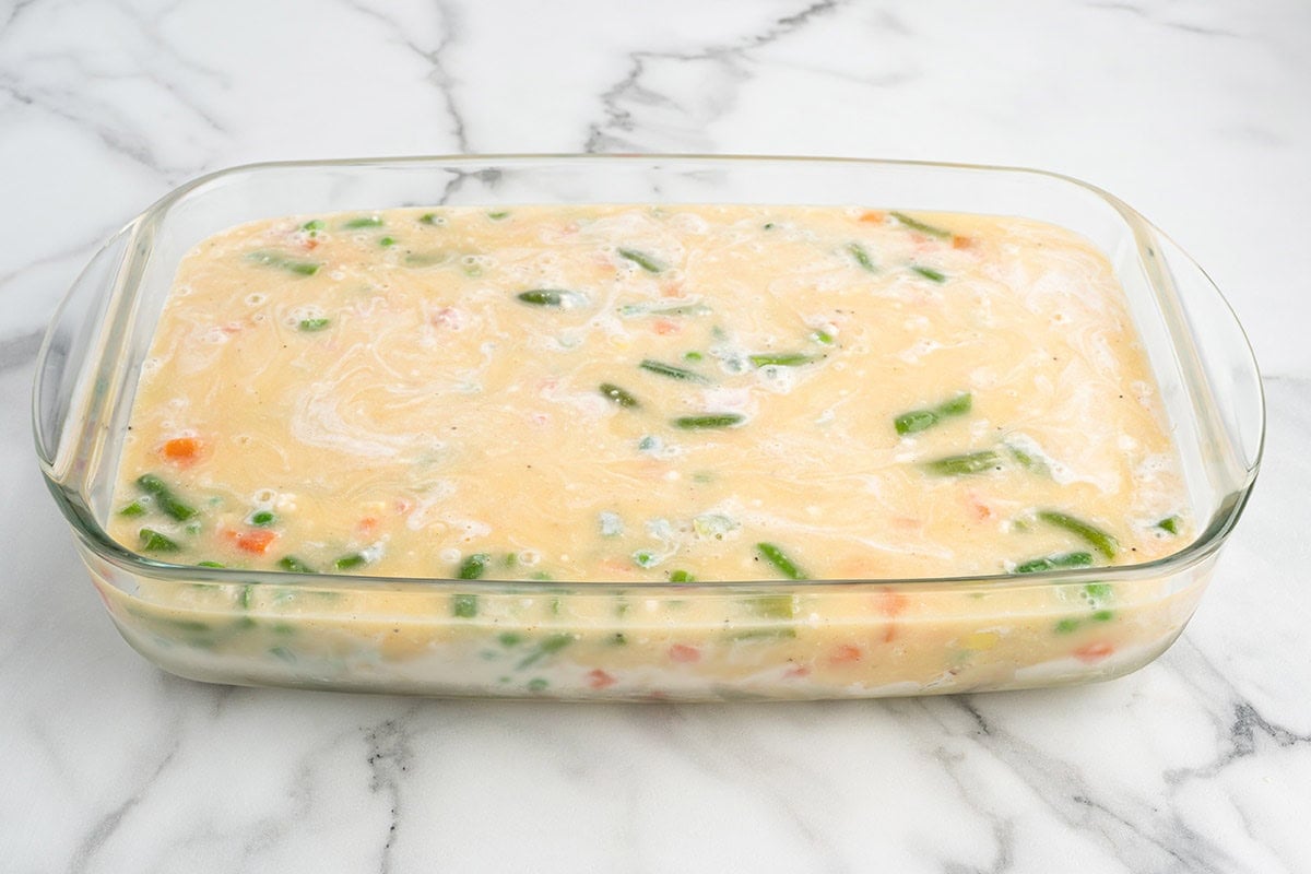Batter topping poured over chicken cobbler filling in a baking dish.