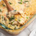 Wooden spoon scooping chicken cobbler with vegetables from a baking dish.