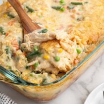 Wooden spoon scooping chicken cobbler with vegetables from a baking dish.