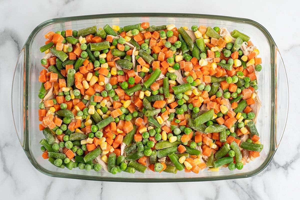 Frozen mixed vegetables layered over chicken in a baking dish.