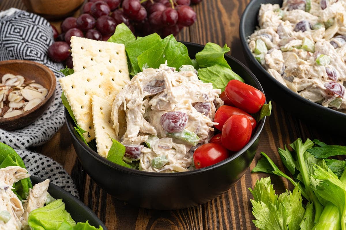 Chicken salad with grapes served in a bowl with crackers, lettuce, and cherry tomatoes.