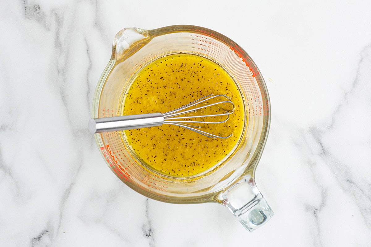 Homemade lemon vinaigrette with herbs and seasonings being whisked in a glass measuring cup.