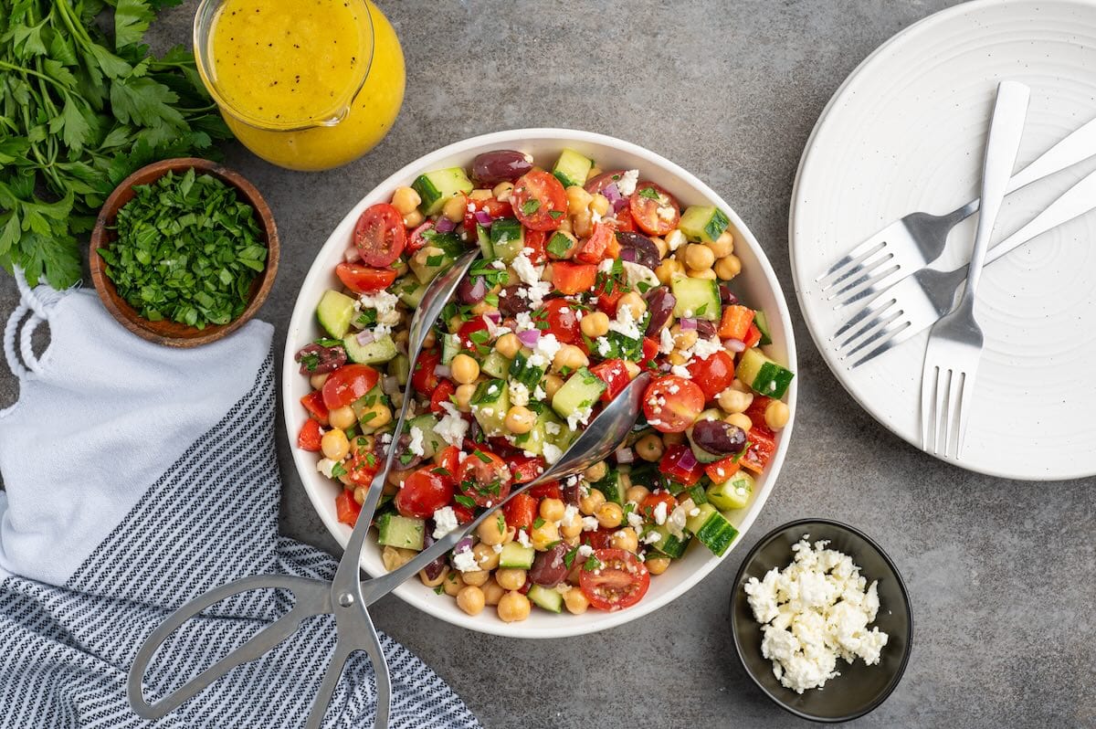 chickpea salad in a white bowl with metal tongs.