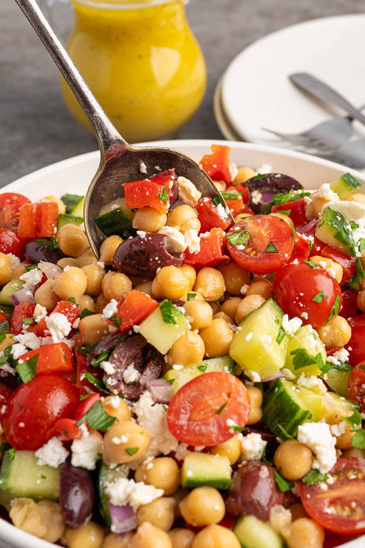 Close-up of chickpea salad with cucumbers, tomatoes, olives, feta, and herbs, served with a spoon.