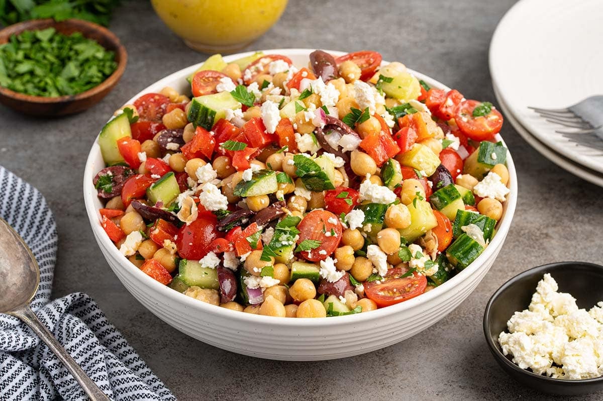 Bowl of Mediterranean chickpea salad with cucumbers, tomatoes, olives, feta, and fresh herbs.