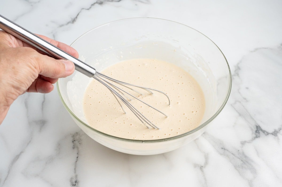 An Oreo cookie being dipped in pancake batter in a glass bowl.