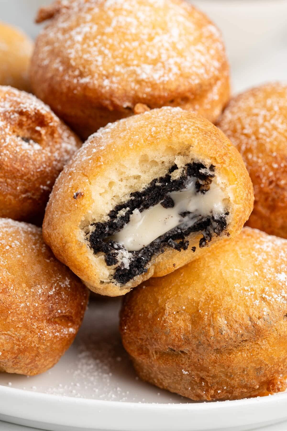 Close-up of a Deep Fried Oreo broken in half showing the melted cream filling and cookie inside, dusted with powdered sugar.