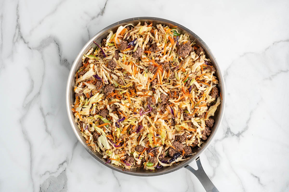 Cooked egg roll in a bowl with ground beef, cabbage, and carrots mixed in a skillet.