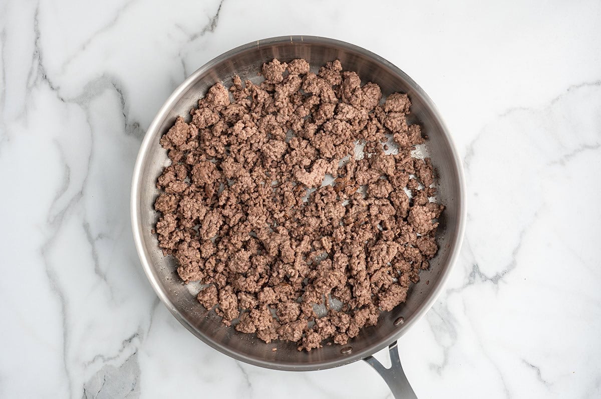 Ground beef cooking in a skillet, browned and crumbled, ready for egg roll in a bowl.