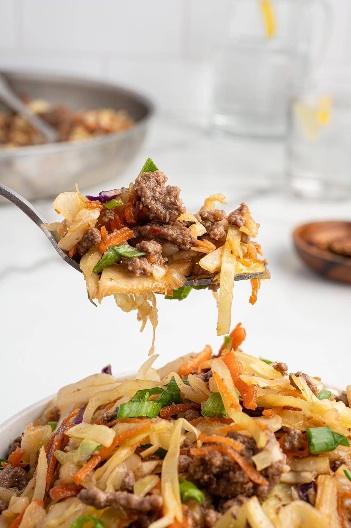 Forkful of egg roll in a bowl with ground beef, cabbage, carrots, and green onions lifted above the dish.