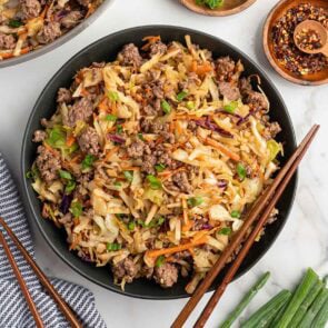 Egg roll in a bowl with ground beef, cabbage, carrots, and green onions served in a black bowl with chopsticks.